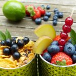 Zwei Gläser mit frischen Früchten, Müsli und Minzblättern, dekoriert mit Beeren, einer Limette und Erdbeeren im Hintergrund für blog Nahrungsergänzungsmittel